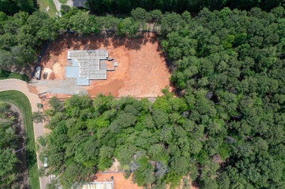 Aerial view of a home foundation under construction on a cleared lot surrounded by trees