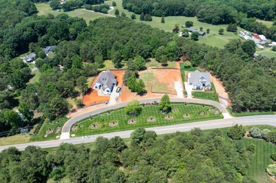 Aerial view of two new homes under construction on large lots with landscaped entrance and surrounding trees