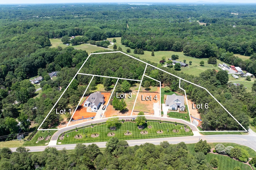Aerial view of residential subdivision with four labeled lots surrounded by trees and green landscaping along a curved road.