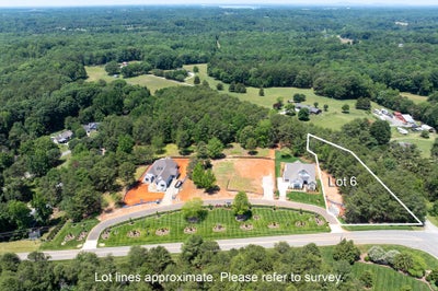 Aerial view of Lot 6, a vacant residential lot beside two homes under construction in a wooded suburban neighborhood.