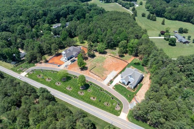 Aerial view of a residential subdivision with two homes, one under construction, on wooded lots along a curved road