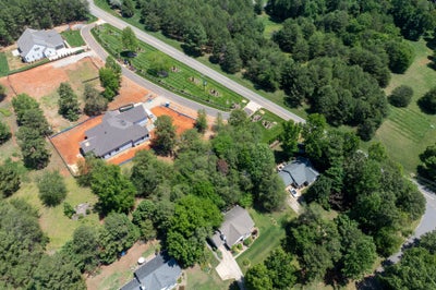 Aerial view of a new home under construction on a cleared lot surrounded by trees and nearby homes