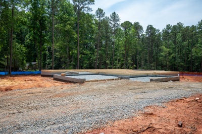 New home construction site showing concrete foundation and wood subfloor framing surrounded by trees