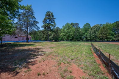 Vacant lot with red clay soil and silt fence beside a home under construction surrounded by trees