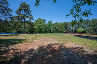 Empty residential lot with cleared land, erosion control fencing, and wooded tree line in background