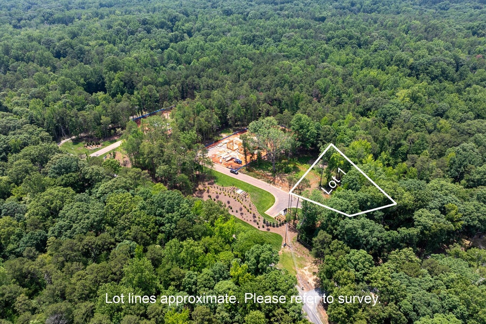 Aerial view of Lot 1, a wooded residential lot with a curved driveway and nearby home under construction.