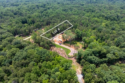 Aerial view of Lot 4 building site surrounded by dense trees with a driveway and home under construction visible.
