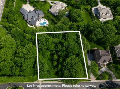 Aerial view of a wooded vacant lot with marked boundaries in a residential neighborhood with large homes nearby.