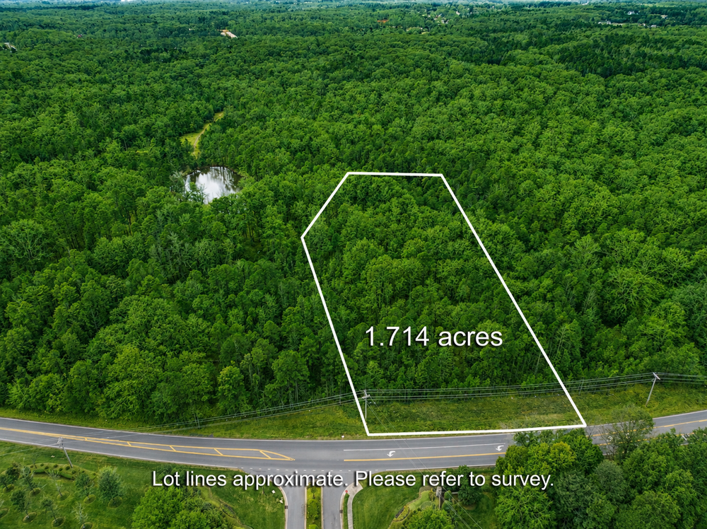 Aerial view of a 1.714-acre wooded lot with marked boundaries along a road, surrounded by trees and a small pond nearby.