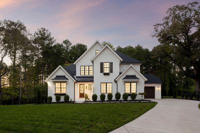 Two-story white brick home with dark roof, black shutters, attached garage, and curved driveway at dusk