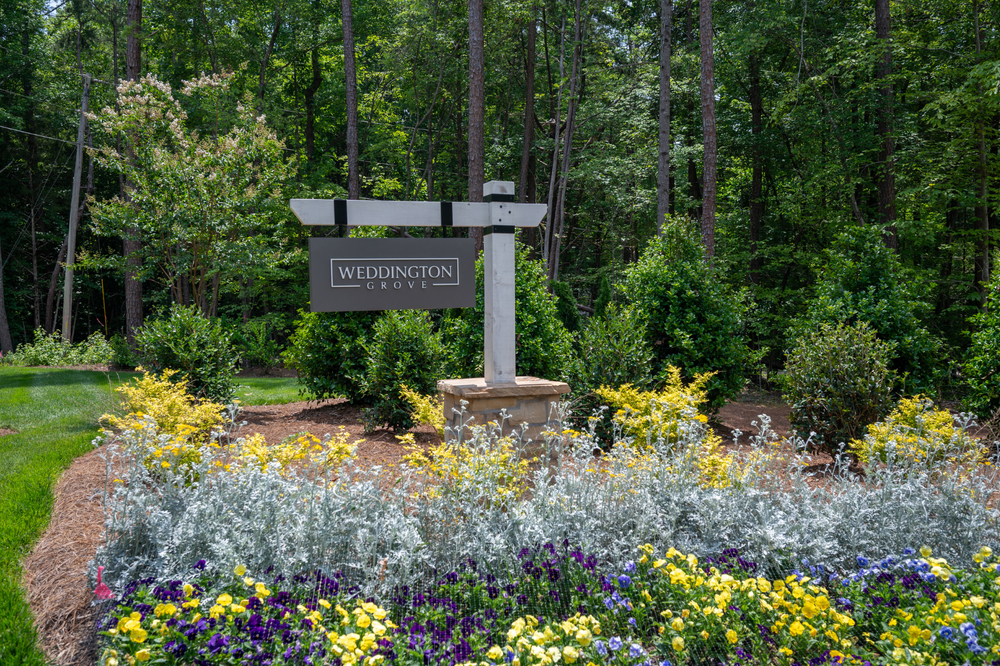 Weddington Grove community entrance sign surrounded by colorful flower beds and mature trees