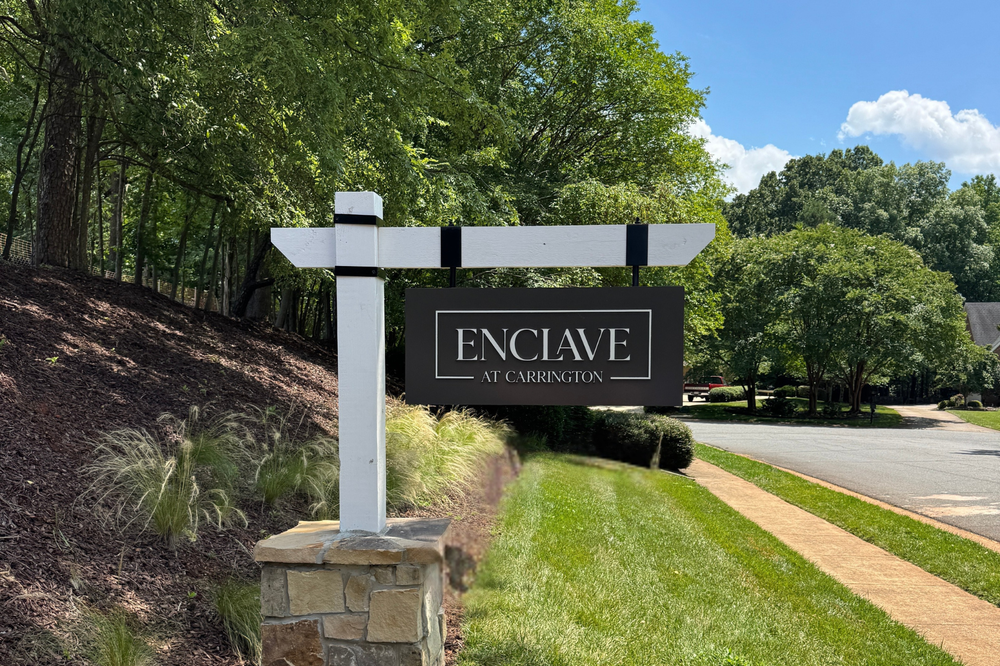 Enclave at Carrington neighborhood entrance sign on a white post with stone base, surrounded by trees and landscaping.