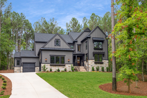 Two-story home with gray board-and-batten siding, stone accents, two-car garage, and wooded lot