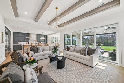 Open living room with exposed beam ceiling, gray sofas, and sliding glass doors leading to a backyard patio