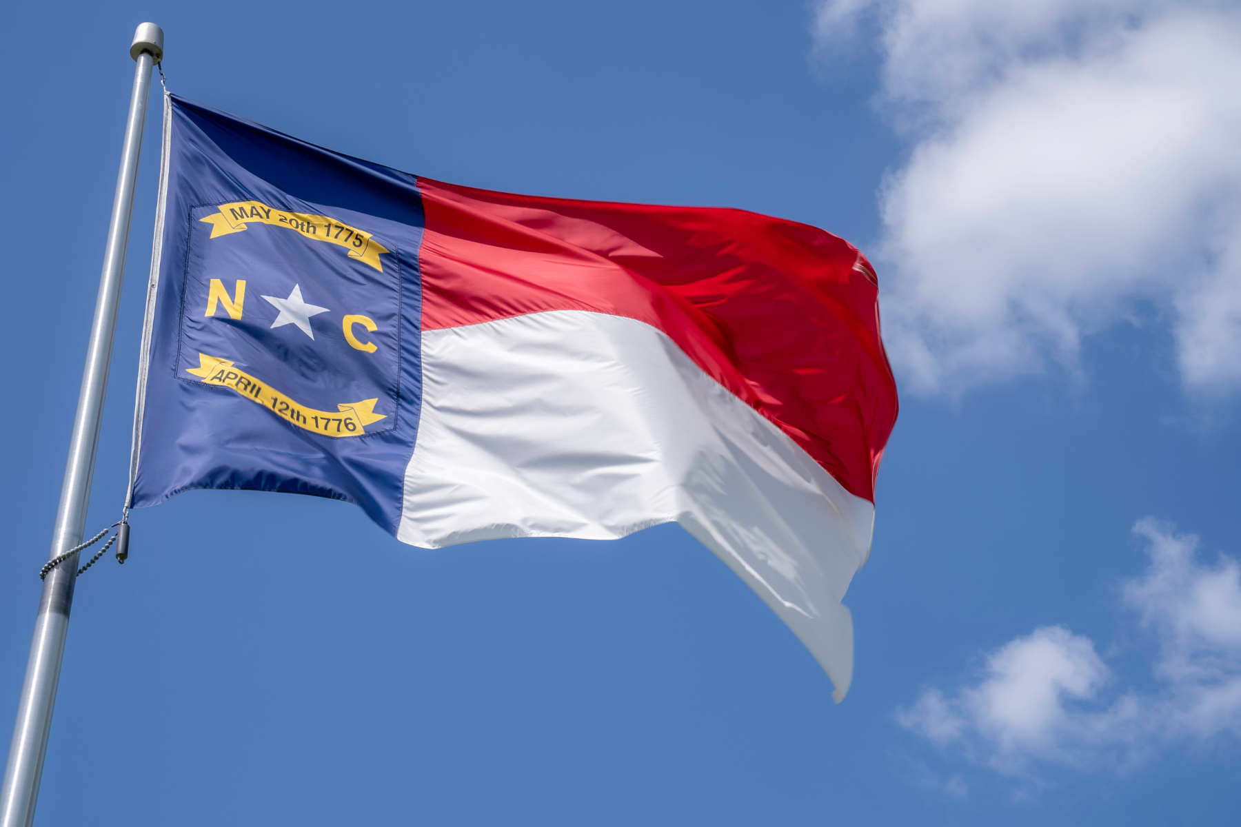 North Carolina state flag with red, white, and blue colors flying on a pole against a blue sky