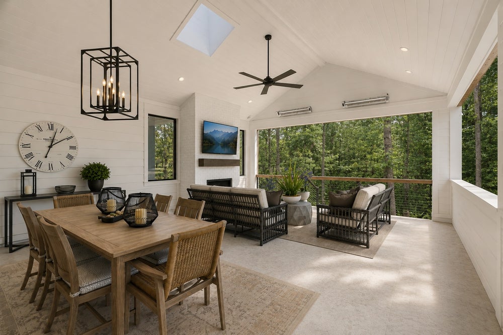 Covered outdoor living space with dining table, fireplace, ceiling fan, and wooded views