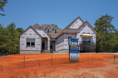 New construction home wrapped in house wrap with a for sale sign on bare dirt lot