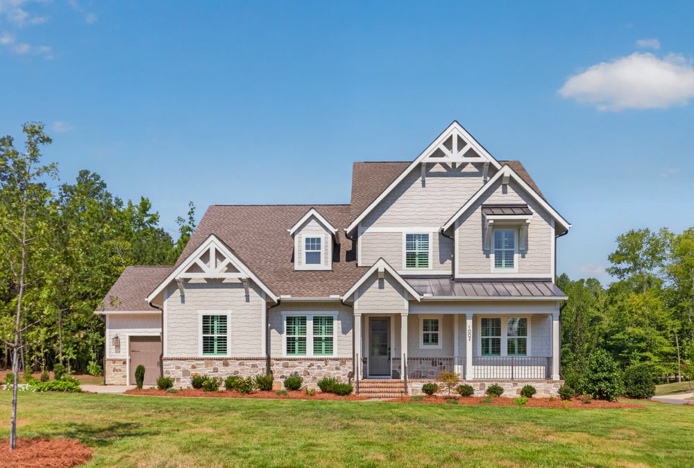 Two-story craftsman home with gray siding, stone foundation, covered porch, and attached garage surrounded by green lawn