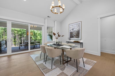 Dining room with glass table, beige chairs, vaulted ceiling, gold chandelier, and sliding doors to outdoor patio