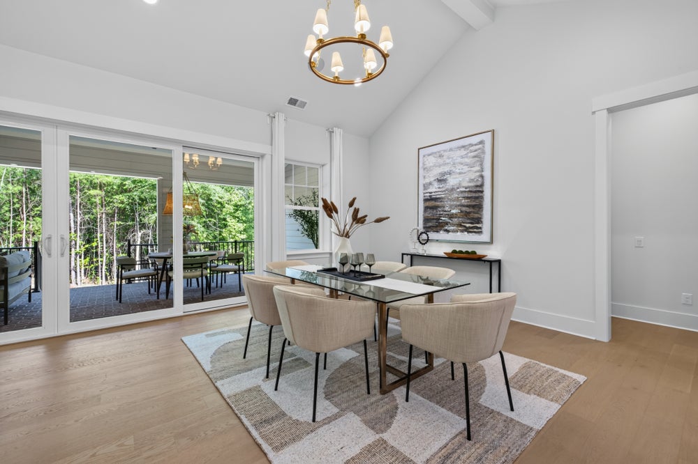 Dining room with glass table, beige chairs, vaulted ceiling, gold chandelier, and sliding doors to outdoor patio
