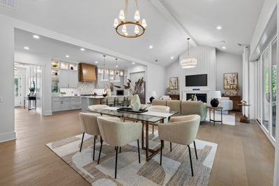 Open-concept dining area with glass table, gold chandelier, and kitchen and living room visible beyond