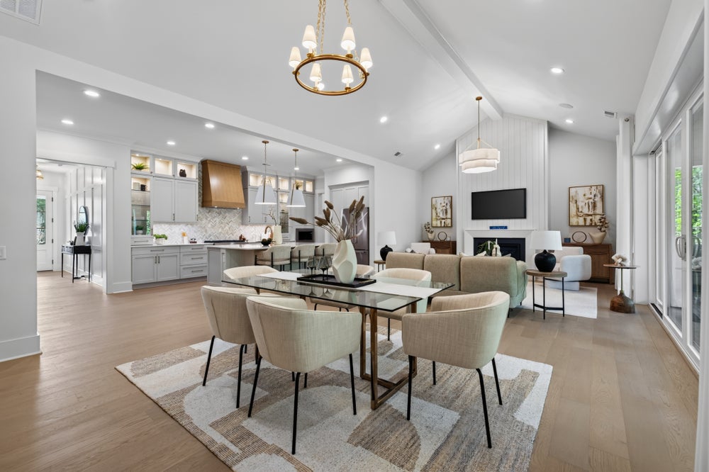Open-concept dining area with glass table, gold chandelier, and kitchen and living room visible beyond