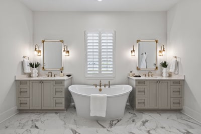 Master bathroom with freestanding soaking tub, dual vanities, marble floors, and gold-framed mirrors