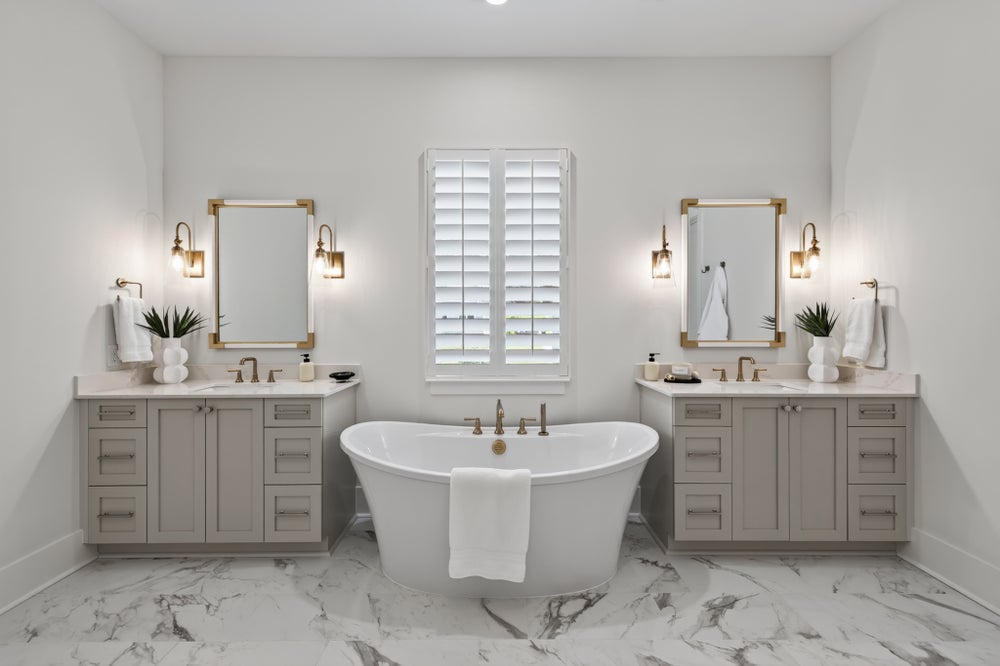 Master bathroom with freestanding soaking tub, dual vanities, marble floors, and gold-framed mirrors