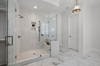 Walk-in shower with white subway tile, glass doors, built-in bench, and marble floors with brass fixtures