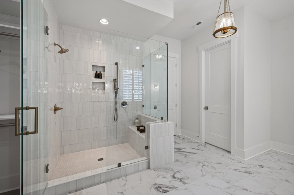 Walk-in shower with white subway tile, glass doors, built-in bench, and marble floors with brass fixtures