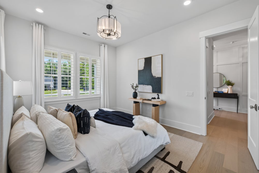 Bedroom with white walls, hardwood floors, pendant light, plantation shutters, and an open door to an ensuite bathroom.