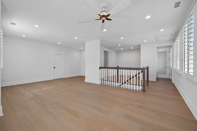 Open upstairs landing with hardwood floors, ceiling fan, stair railing, and plantation shutters on windows