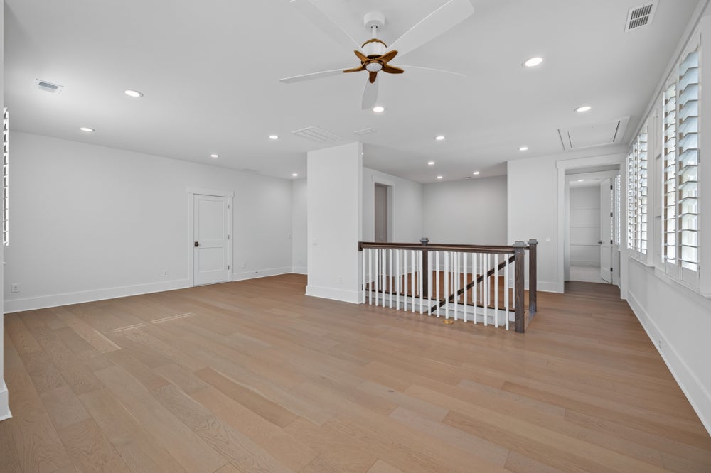 Open upstairs landing with hardwood floors, ceiling fan, stair railing, and plantation shutters on windows