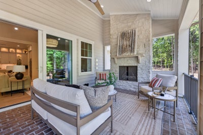 Covered porch with stone fireplace, outdoor seating, brick floor, and sliding glass doors to interior living area.