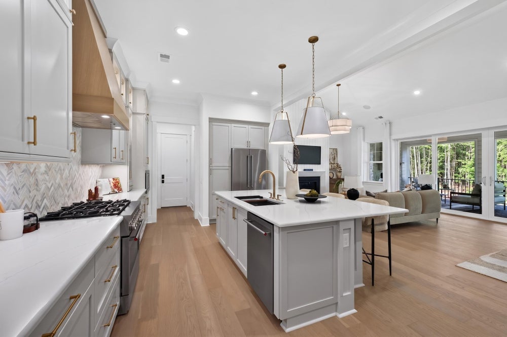Open-concept kitchen with gray cabinets, large island, gas range, and hardwood floors opening to living area