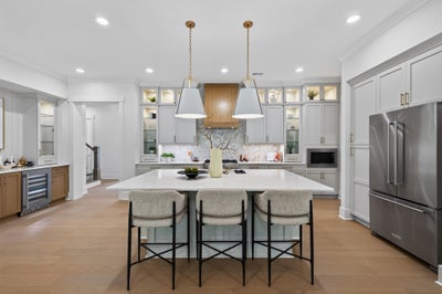 Large kitchen with gray cabinets, center island with three bar stools, pendant lights, and stainless steel refrigerator