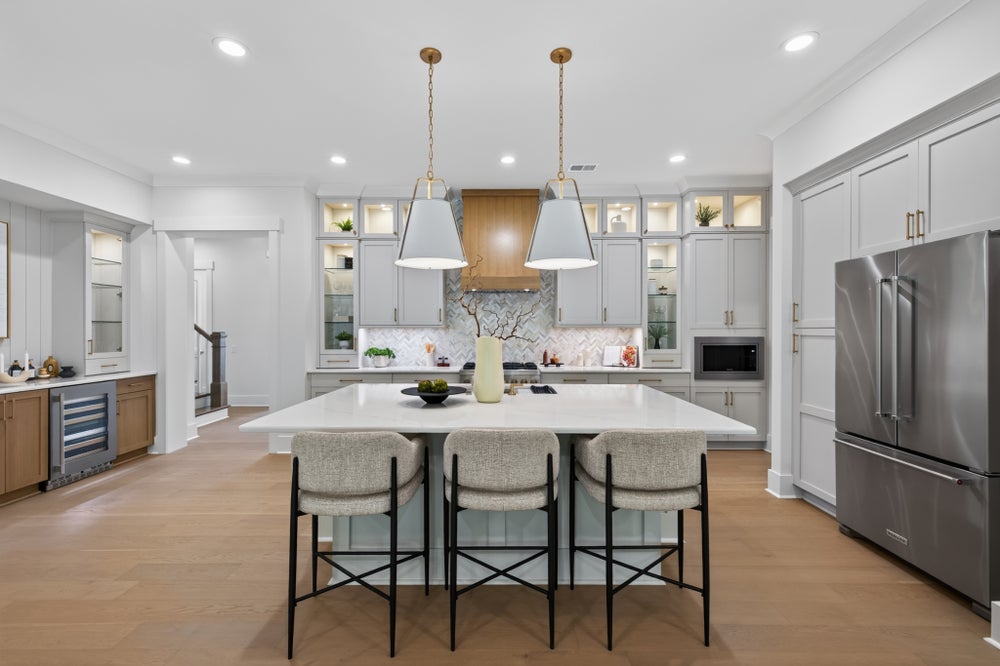 Large kitchen with gray cabinets, center island with three bar stools, pendant lights, and stainless steel refrigerator