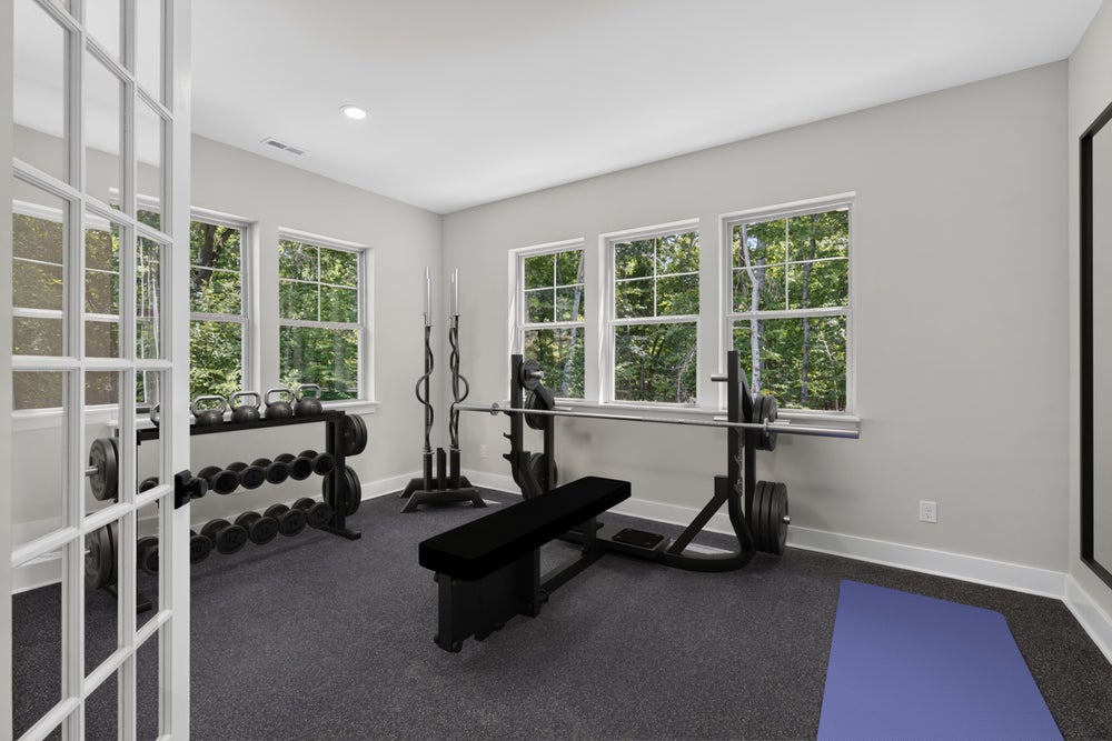 Home gym with bench press, dumbbell rack, kettlebells, and yoga mat on dark carpet flooring
