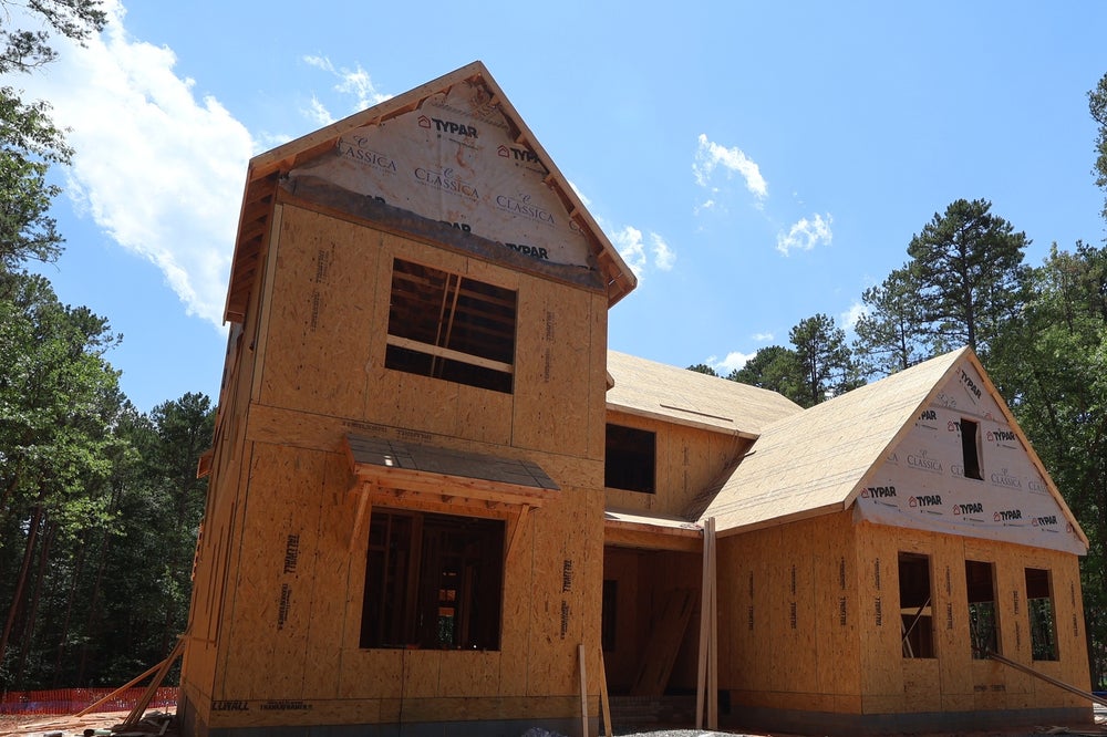 Two-story home under construction showing wood framing and house wrap exterior with roofline visible