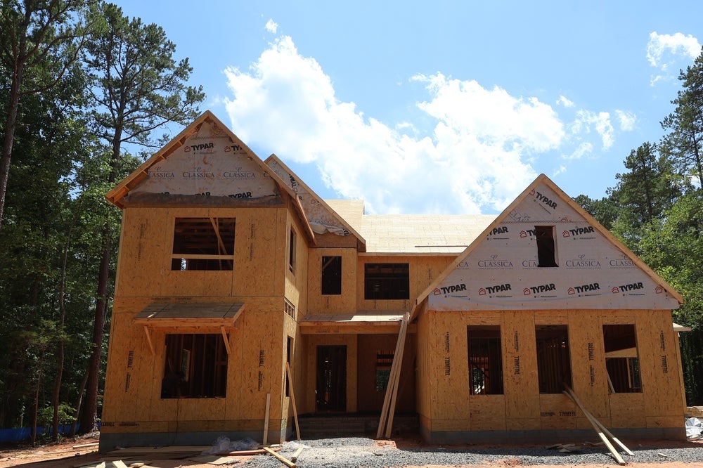 Two-story home under construction showing wood framing, house wrap, and roof sheathing with multiple gabled peaks