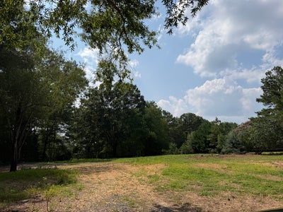 Open residential lot with cleared ground, surrounded by mature trees under a partly cloudy sky