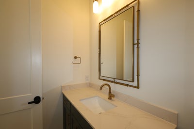Bathroom vanity with marble countertop, dark cabinets, gold faucet, and framed mirror above single sink