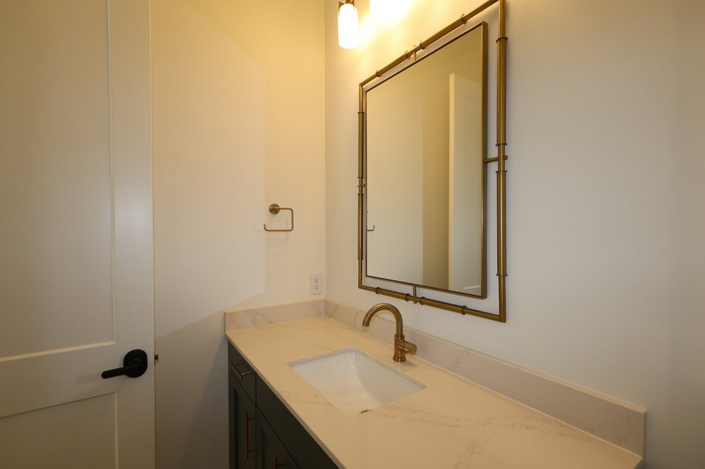 Bathroom vanity with marble countertop, dark cabinets, gold faucet, and framed mirror above single sink
