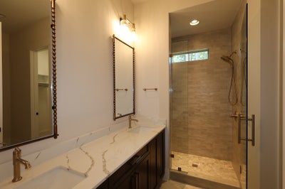 Bathroom with double vanity, marble countertop, dark cabinets, and glass-enclosed tile shower with brass fixtures