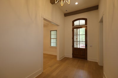 Foyer with arched wood front door, exposed ceiling beams, hardwood floors, and gold chandelier