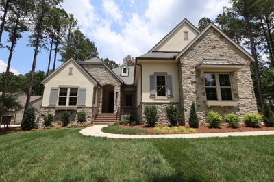 Single-story home with stone and stucco exterior, gray shutters, arched entry, and landscaped front yard surrounded by trees