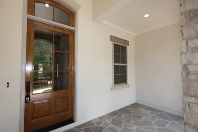 Covered front entry with wood and glass door, arched transom, stone column, and slate tile floor