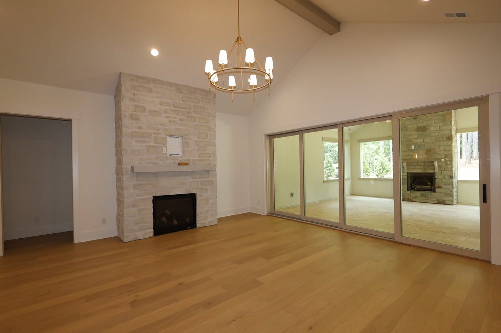 Open living room with vaulted ceiling, stone fireplace, hardwood floors, and sliding glass doors