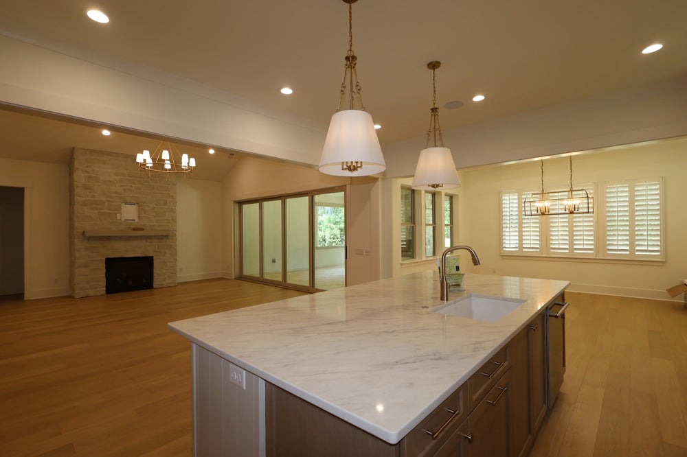 Large kitchen island with marble countertop and sink, open to living room with stone fireplace and hardwood floors