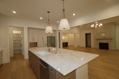 Large kitchen island with marble countertop and sink, open to living room with stone fireplace and hardwood floors